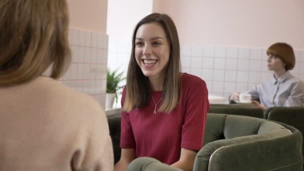 Três jovens caucasianas sentadas em um café e sorrindo, conversando, dialogando, emoção de surpresa, conceito de fofoca. Antecedentes 60 fps — Vídeo de Stock