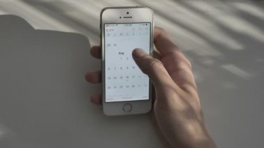 Mens yazarak, güneş ışığı ekran, yansıma, kavramı üzerinde beyaz bir akıllı telefon üzerinde kayan takvim ver. Güneşli bir tablo içinde belgili tanımlık geçmiş. 60 fps