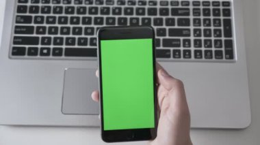Erkek ellerini bir daha büyük siyah smartphone, arka planda laptpo dokunun. Yeşil ekran, chromakey kavramı, laptop içinde belgili tanımlık geçmiş. 60 fps vurdu top