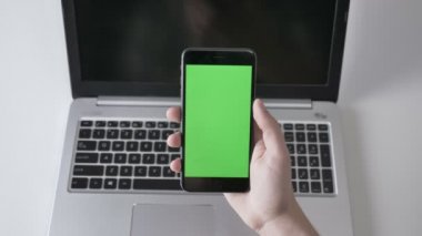 Erkek ellerini bir daha büyük siyah smartphone, arka planda laptpo dokunun. Yeşil ekran, chromakey kavramı, laptop içinde belgili tanımlık geçmiş. 60 fps vurdu top