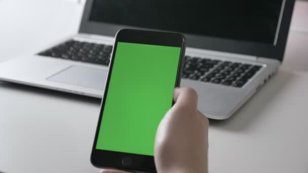 Мужские руки держат большой черный смартфон жест крана. Зеленый экран, концепция хромакея, ноутбук в фоновом режиме 60 кадров в секунду — стоковое видео