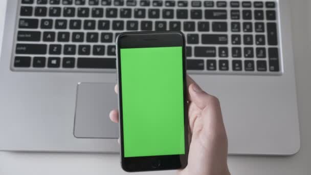 Manliga händer tryck på en större svart smartphone, laptpo i bakgrunden. Grön skärm, chromakey koncept, laptop i bakgrunden. Topp skott 60 fps — Stockvideo