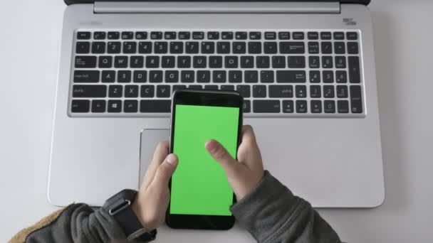 As mãos das crianças usam um smartphone, tela verde, conceito de chromakey, laptop em segundo plano. Tiro superior 60 fps — Vídeo de Stock