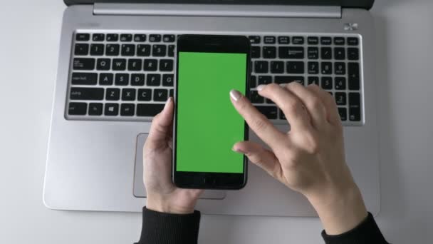 Női kezek az okostelefonok érintőképernyős görgetést. Zöld képernyő chroma-key koncepció, laptop a háttérben. Top shot 60 fps — Stock videók