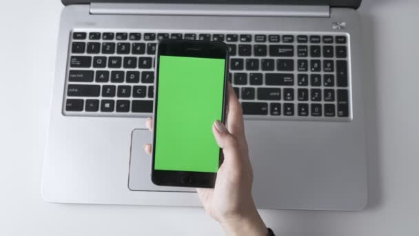 Vrouwelijke handen veeg over het touchscreen smartphones. Groen scherm, chromakey concept, laptop op de achtergrond. Top shot van 60 beelden per seconde — Stockvideo