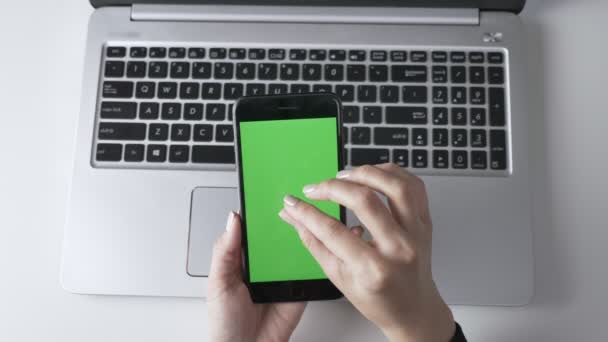 Vrouwelijke handen knijpen om in te zoomen op de touchscreen smartphones doet. Groen scherm, chromakey concept, laptop op de achtergrond. Top shot van 60 beelden per seconde — Stockvideo