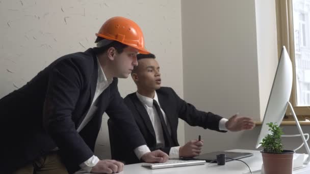 Dois jovens empresários, arquiteto, discutem o projeto e olham para o monitor no escritório. Construtores, engenheiros, conceito. 60 fps — Vídeo de Stock