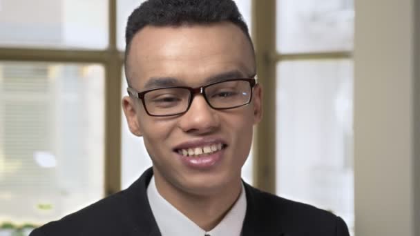 Joven empresario africano exitoso mirando a la cámara y sonriendo, retrato en la oficina en el fondo 60 fps — Vídeos de Stock