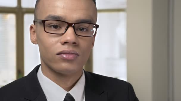 Der junge erfolgreiche afrikanische Geschäftsmann blickt mit ernstem Gesicht in die Kamera, im Hintergrund ein trauriges Porträt im Büro. 60 fps — Stockvideo