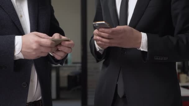 Two businessmen in suits stand in the office and using smartphones. 60 fps — Stock Video