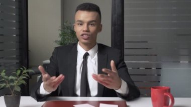 Genç başarılı bir Afrika iş adamı ofiste oturan ve kameraya bakarken konuşuyor. Onun jestlerle 60 fps eller