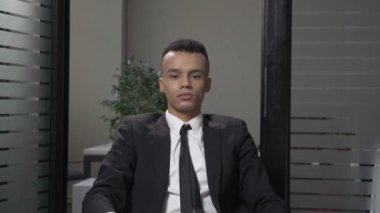 Elbiseli genç başarılı Afrika iş adamı ciddi bir yüz ofiste oturan bir bok işaretleri gösteriyor. 60 fps