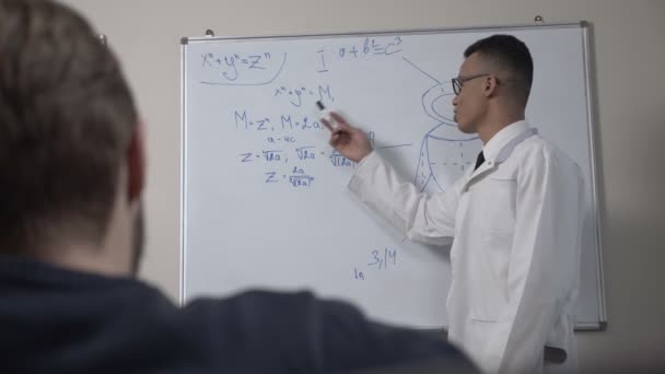 Ένα νεαρό επιστήμονα επιτυχημένη Αφρικής σε ένα άσπρο παλτό και γυαλιά, στέκεται στο μαυροπίνακα με φόρμουλες, διάλεξη, παρουσίαση, εκπαιδευτική ιδέα. 60 fps — Αρχείο Βίντεο