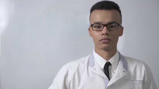 Jovem cientista africano bem sucedido com um casaco branco e óculos mostrando um sinal de como, olha para a câmera, conceito retrato. 60 fps — Vídeo de Stock