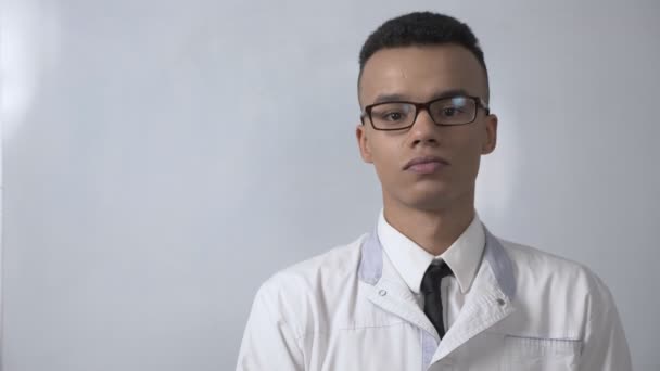 Sim, balançando a cabeça, gesto de jovem cientista africano bem sucedido com um casaco branco e óculos olha para a câmera, conceito retrato. 60 fps — Vídeo de Stock