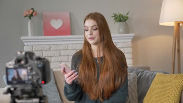 Jonge roodharige meisje blogger, glimlachen, praten op de camera, met behulp van een smartphone, lezen van commentaren, home comfort op de achtergrond. 60 fps — Stockvideo