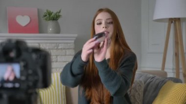 Kızıl saçlı kız blogger, gülümseyen, kameraya konuşurken, yeni bir satın alma, ruj, allık, toz, makyaj kavramı, ev konfor kozmetik arka planda gösterilen. 60 fps