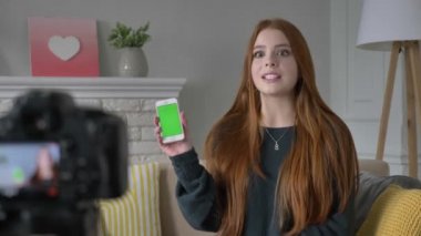 Kızıl saçlı kız blogger, gülümseyen, kameraya konuşurken, bir yeni satın alma, smartphone, uygulama, yeşil ekran, chroma key, ev konfor arka planda gösterilen. 60 fps