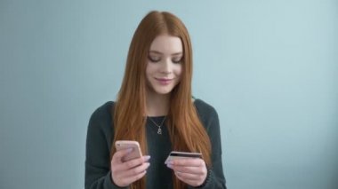 Genç güzel kızıl saçlı kız bir satın alma online, yaşam tarzı, bu evde kredi kartı ile alışveriş online smartphone kullanarak online bankacılık yapar. teknoloji ve internet kavramı 60 fps