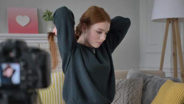 Fiatal vörös hajú lány blogger, mosolyogva, beszél a kamera teszi magát a frizura, tress, otthoni kényelmet a háttérben. 60 fps — Stock videók