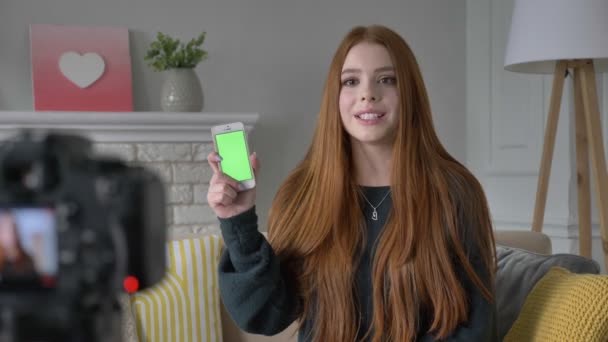 Jonge roodharige meisje blogger, glimlachen, praten op de camera, een nieuwe aankoop, smartphone, application, groen scherm, Chromakey, home comfort in de achtergrond tonen. 60 fps — Stockvideo