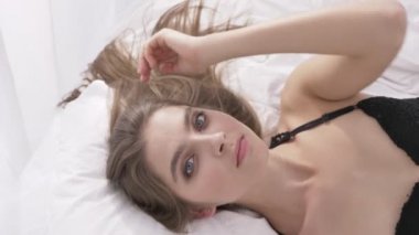 Genç Beyaz sarışın kız seksi siyah iç çamaşırı yalanlar üzerine bir yatak ve gülümseyen, fotoğraf, portre, günaha bakar, güneş ışığı, en iyi arka planda vurdu kavramı 60 fps