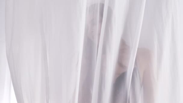 Joven rubia caucásica en lencería sexy para tocar la cortina, tul y mira a la cámara, Retrato, seducción, luz solar en el fondo, concepto de silueta, primer plano 60 fps — Vídeos de Stock