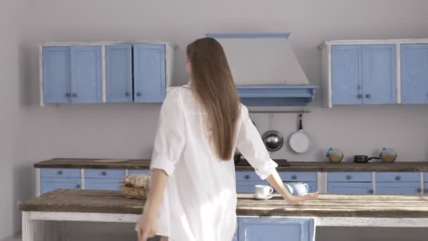 Joven hermosa chica caucásica sexy en camisa blanca, lencería negra caminando por la cocina, sonriendo, tentación, sexy, luz del sol blanca en el fondo. 60 fps — Vídeos de Stock