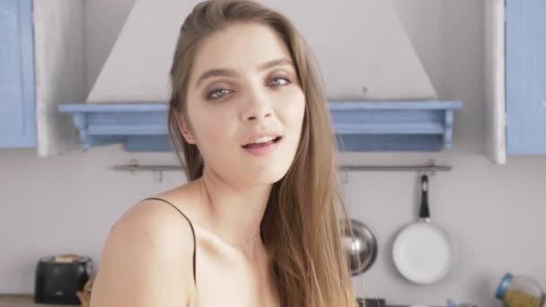 Porträtt av en ung sexig kaukasisk kvinna i svart underkläder tittar på kameran, kök i bakgrunden, närbild med 50 fps — Stockvideo