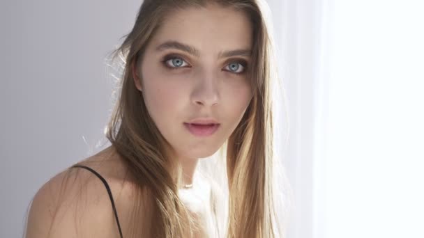 Young beautiful caucasian girl looks surprised at camera, portrait, daylight, near window, curtain 50 fps — Stock Video