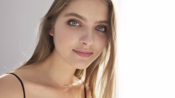 Young beautiful caucasian girl looking into the camera, winking, flirting, portrait, sunlight, near the window, curtain 50 fps — Stock Video