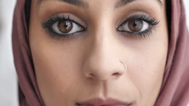 Close-up of female Indian sad eyes. Young beautiful serious Indian girl in pink hijab looking at camera. Portrait, white background, close up 60 fps — Stock Video