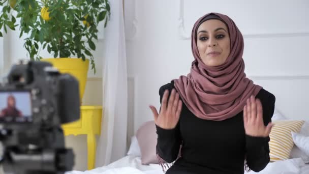 Menina indiana bonita nova no blogueiro hijab falando na câmera, diz subscrever o canal, como, repost, sala branca, conforto em casa no fundo. 50 fps — Vídeo de Stock
