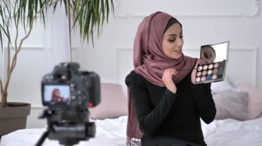 Gülümseyerek, yeni bir satın alma, gösterilen genç güzel Hint kızı kameraya konuşurken hijab blogger kozmetik, göz farı palet, ev konforu içinde belgili tanımlık geçmiş. 60 fps
