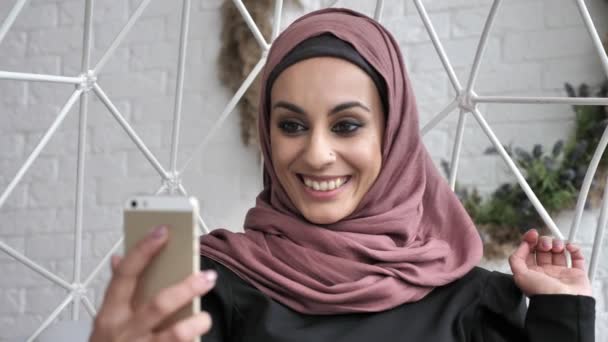 Fiatal gyönyörű indiai lány visel a hidzsáb, mosolyogva, ezzel a selfie, integetett a kezét, üdvözlő mozdulattal, viszlát 50 fps — Stock videók