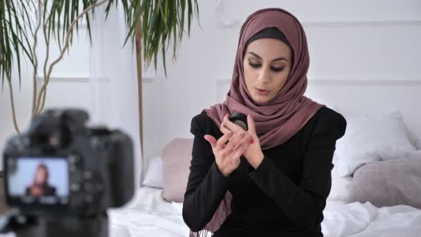 Gülümseyerek, yeni bir satın alma, aquagrum, ev konfor kozmetik arka planda gösterilen genç güzel Hint kızı kameraya konuşurken hijab blogger. 60 fps — Stok video