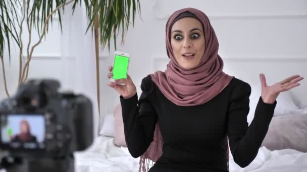 Menina indiana bonita nova no hijab recomenda uma aplicação em um smartphone, sorrindo, falando para a câmera, chave chroma, conceito de tela verde. 50 fps — Vídeo de Stock