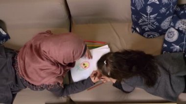 Müslüman anne ve kızı koltukta yalan ve 50 fps görüntülemek vurdu boya ile renkli kalemler, arka plan, en iyi ev rahatlığında