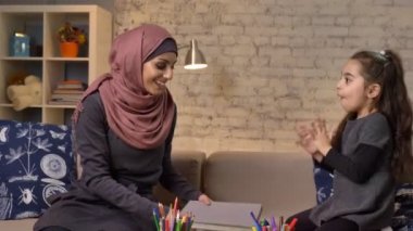 Genç Müslüman anne onu kızım onun elinde bir kitap heyecanla gülüyor ve onu gürlemesi hijab alır 50 fps eller