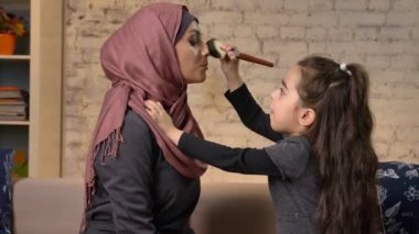 Küçük kızı gülen, gülümseyen aile, İdil, ev konfor içinde belgili tanımlık geçmiş Müslüman annesi için hijab, makyaj fırça, içinde bir makyaj yapan 50 fps