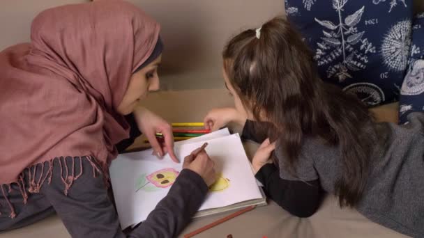 Muslimische Mutter und Tochter liegen auf dem Sofa und malen mit Buntstiften, Wohnkomfort im Hintergrund, Seitenansicht 50 fps — Stockvideo