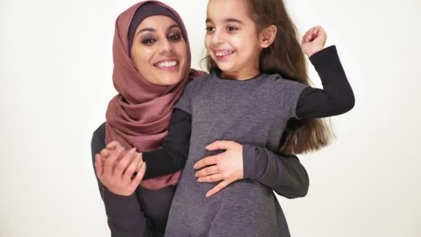 Jonge mooie moeder in hijab hugs haar dochtertje, familie, gelukkig familie concept, idylle lachen, kijken camera, witte achtergrond 50 fps — Stockvideo