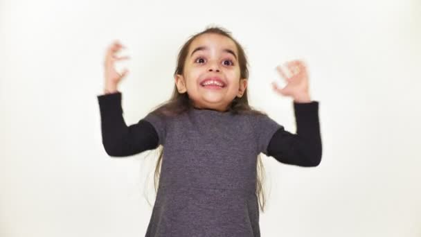 Pequena menina doce bonita está feliz, sorrindo, alegrando-se, levanta os braços para o topo, surpreso, fundo branco, fundo branco 50 fps — Vídeo de Stock