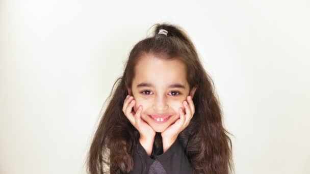 Little cute caucasian girl, smiling, showing an emotion of expectation, holding her head with her hands, portrait white background 50 fps — Stock Video