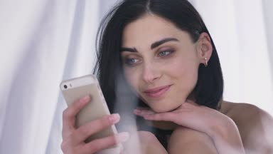 Genç seksi beyaz esmer kız kadın iç çamaşırı tutar baş el ile smartphone okuma, gülümseyen, kullanarak portresi beyaz arka plan 50 fps