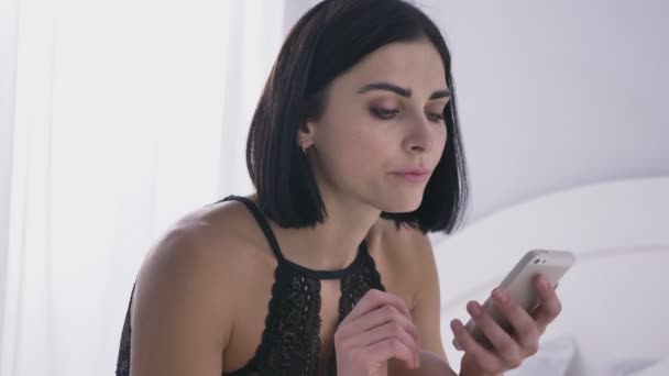 Portret van jonge sexy Kaukasische brunette meisje in lingerie met behulp van de smartphone, lezen, jatten, witte achtergrond 50 fps — Stockvideo