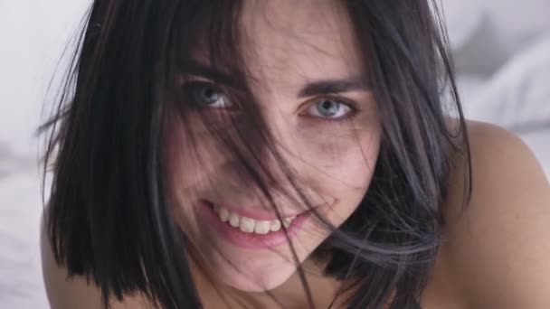 Porträtt av en ung kaukasiska brunett flicka, tittar på kameran, blå ögon, leende, skakar huvud. — Stockvideo