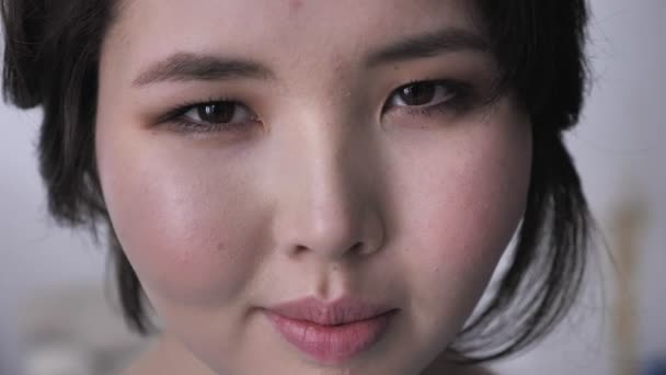 Gülümseyerek, yanıp sönen kameraya, ciddi bir yüz, arayan genç Asyalı esmer kız, portresi. 50 fps — Stok video