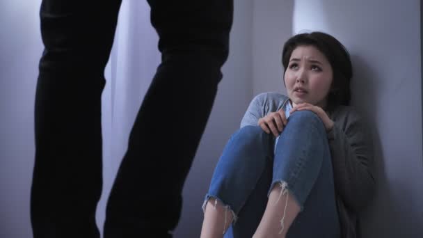 Грустная азиатка сидит на полу, злой муж угрожает, конфликт в семье, насилие 50 кадров в секунду — стоковое видео