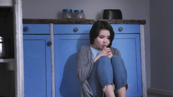 Dizlerinin silah, Aile içi şiddet kavramı ile tutarak mutfak, yerde oturan üzgün yalnız genç Asyalı kız 50 fps — Stok video